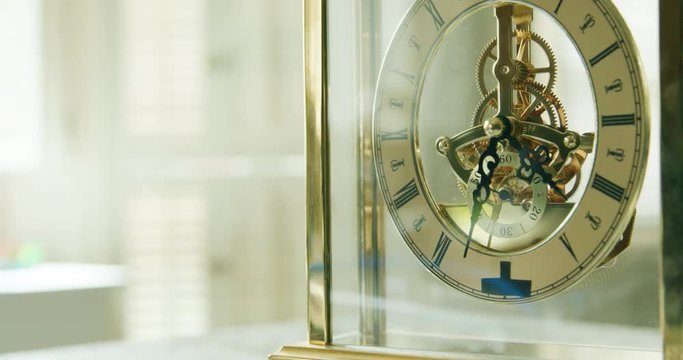 Sunshine filters through the glass enclosure to the internal workings of a lovely bright brass mechanical table clock.