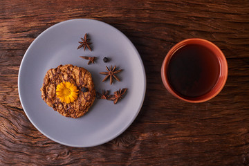 Cup of black tea and chocolate coockies with yellow flower on top on wooden table on black background