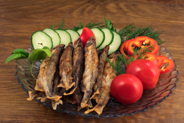 Sea fish, fried in oil, lined with a slide on a plate with a side dish of fresh vegetables, dill...