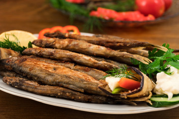 Fish dish of whole fried capelin with garnish of stuffed eggplant, sour cream, cucumber slices and parsley.