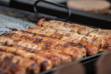 Bacon wrapped hotdogs cooking on the outdoor grill at country fair for hungry customers.