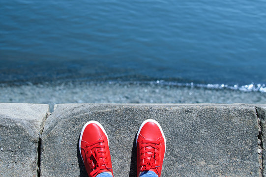 Legs in red sneakers stand on the edge. View of the sea.