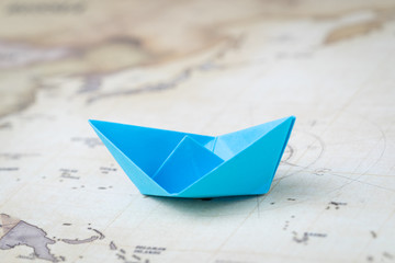 Blue origami paper ship or boat on vintage ocean map with printed compass, travel, sail or cruise concept, shipping or transportation through the sea.