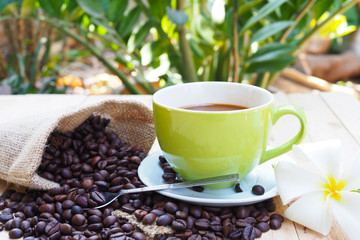 Green coffee cup with burlap sack of coffee beans on wooden table