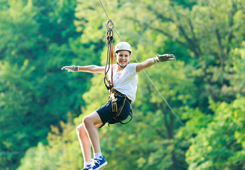 Happy, cute, young boy in white t shirt and helmet having fun and playing at adventure park,...