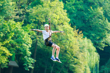 Happy, cute, young boy in white t shirt and helmet having fun and playing at adventure park, holding ropes and climbing wooden stairs. active lifestyle concept