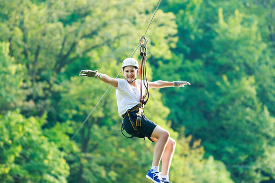 Happy, cute, young boy in white t shirt and helmet having fun and playing at adventure park, holding ropes and climbing wooden stairs. active lifestyle concept