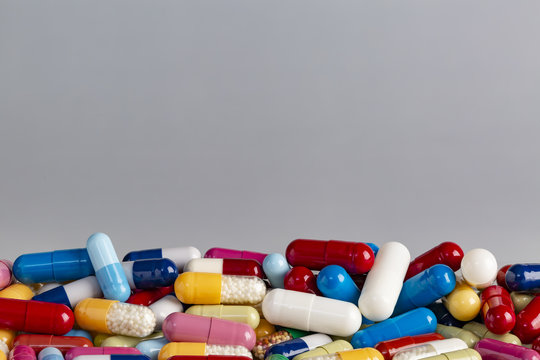 Color capsules and pills on grey background, top view copy space