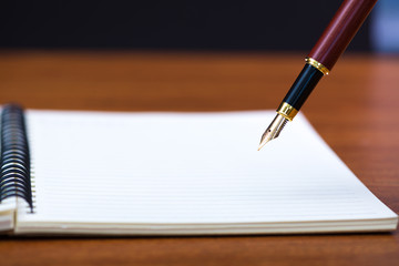 Close up of fountain pen or ink pen with notebook paper on wooden working table with copy space,...
