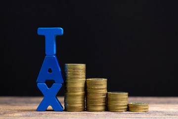 TAX concept. TAX alphabet with stack of coin on wooden working table in dark background, business...