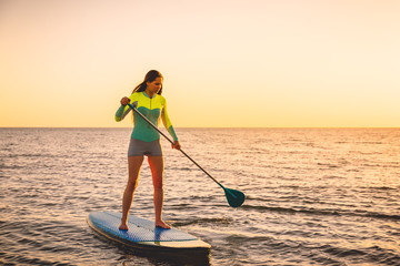 Attractive young woman at stand up paddle board with sunset colors