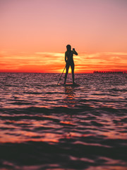 Sporty woman stand up paddle boarding  on a flat warm quiet sea with bright sunset