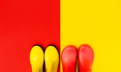Red rubber boots on a yellow background and yellow boots on a red background stand side by side. The concept of "Autumn is coming". Top view