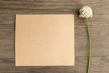 Wild garlic white flowers with craft paper blank on old grunge wooden background. Top view. Minimalistic mockup.