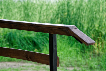 Wooden handrail in Public park with lawn bench and green tree, place for relaxation.