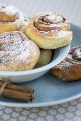 Cinnamon snails called kanelbullar, very tasty sweet rolls in blue bowl on floral pattern tablecloth, raw cinnamon
