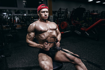 Fototapeta na wymiar Muscular athletic bodybuilder fitness model posing and exercises in gym