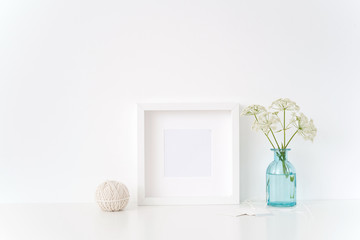 White square frame mock up with a summer herbal gerard in transparent blue vase on white background. Mockup for quote, promotion, headline, design.