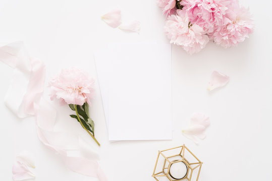 Elegant feminine wedding or birthday flat lay composition with pink peonies floral bouquet, silk ribbon and candle Blank paper card, mockup, invitations. Flatlay, top view.
