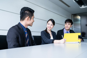Confident businesswoman sitting at table and signing paperwork of his partner and smiling after...