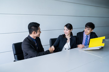 Confident businesswoman sitting at table and  shaking hand and signing paperwork of his partner and...