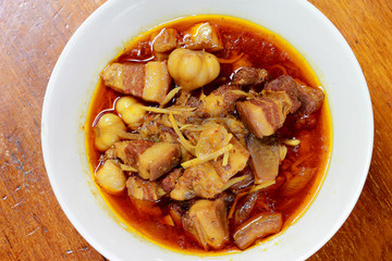 Northern Thailand local dish called Gaaeng Hang Laeh Moo is a Northern Style Hang Lay Curry with Thai herb, streaky pork, pickled onions in a bowl on wooden table. Thai traditional local northern food