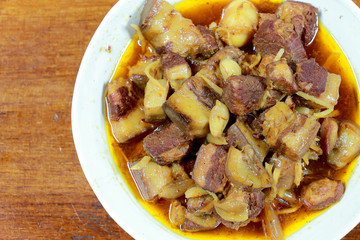 Northern Thailand local dish called Gaaeng Hang Laeh Moo is a Northern Style Hang Lay Curry with Thai herb, streaky pork, pickled onions in a bowl on wooden table. Thai traditional local northern food