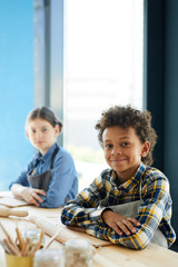 Mixed-race pupil and his classmate sitting by desk at lesson of craftsmanship