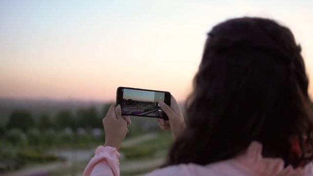 A girl with long hair takes a photo of the city using a smartphone. slow motion.