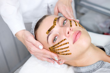 Cosmetologist making taping face procedure using tiger colored tapes in beauty parlor