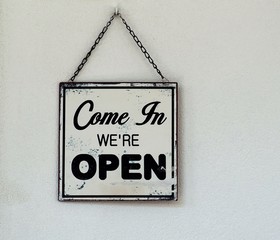 Come in we are open,  black and white  retro sign on white wall of a store.