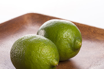 two fresh green limes on the wood tray isolated white