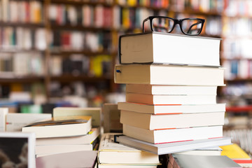 glasses on top of stack of books lying on table in bookstore