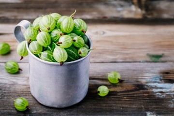 Fresh raw green gooseberries in a mug on wooden background.