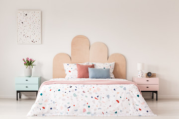 Patterned bed with headboard between pink and blue cabinet in bedroom interior with poster. Real photo