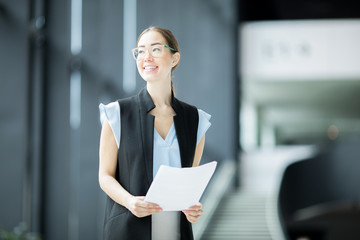 Cheerful economist with documents looking aside while preparing with her working report