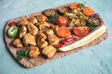 Grilled chicken pieces with vegetables on thin bread.
