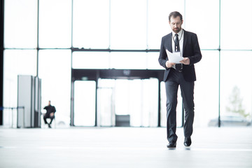 Young well-dressed delegate moving inside lounge of airport and looking through papers