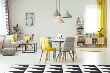 Real photo of a modern dining room interior with a yellow chair, table, pastel lamps and geometrical carpet