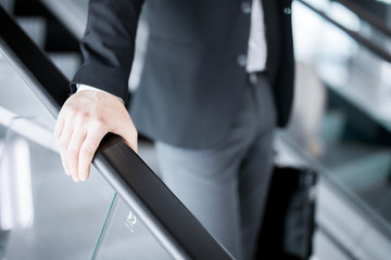 Hand of young businessman on railings of escalator during motion downwards