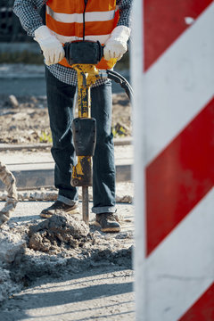 Worker in reflective vest and with drill repairing asphalt during roadworks