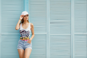 Fototapeta premium Outdoor lifestyle portrait of hipster girl posing near pool, wearing bright swag clothes. Ready for pool party, sexy tanned body and long legs, enjoy tropical vacation.
