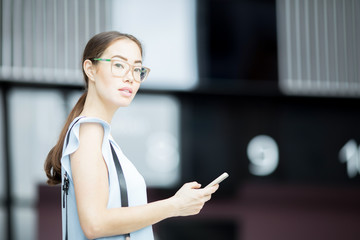 Young serious employee with smartphone looking at you while messaging on the move