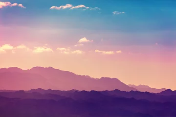 Poster Zonsondergang over bergen. Silhouet van een bergketen tegen de hemel bij zonsondergang © vvvita