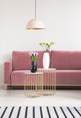 Golden small tables with flowers, pink couch and chandelier in a living room interior. Real photo