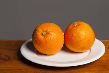 fresh orange closeup on the dish, wood table, grey background.