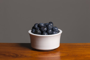 blue barry on the white ceramic, wood table, grey background.
