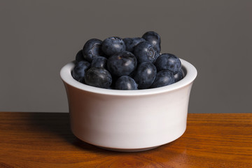 blue barry on the white ceramic, wood table, grey background.