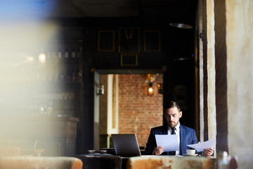 Serious concentrated handsome business analyst in formal jacket examining report or reading...