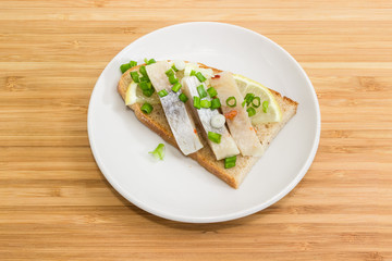 Open sandwich with pickled herring slices and lemon on saucer